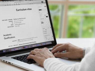 A person editing a CV on a laptop with a globe and passport nearby, featuring text "How to Write a Winning CV for International Jobs."