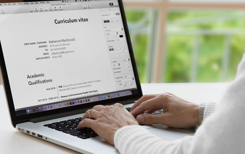A person editing a CV on a laptop with a globe and passport nearby, featuring text "How to Write a Winning CV for International Jobs."