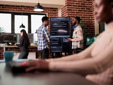 A group of diverse professionals in a modern office with a laptop and company logos, featuring text "Top 7 Companies Visa Sponsorship Jobs."