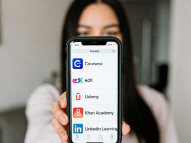 Young student holding up a smartphone showing the apps of top online learning platforms: Coursera, edX, Udemy, Khan Academy, and LinkedIn Learning.