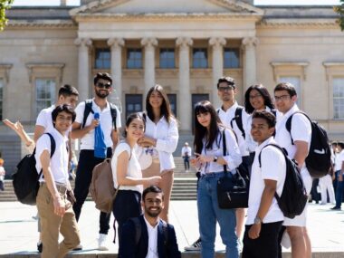 Diverse group of happy international students smiling on university steps, representing affordable countries to study abroad in 2025.
