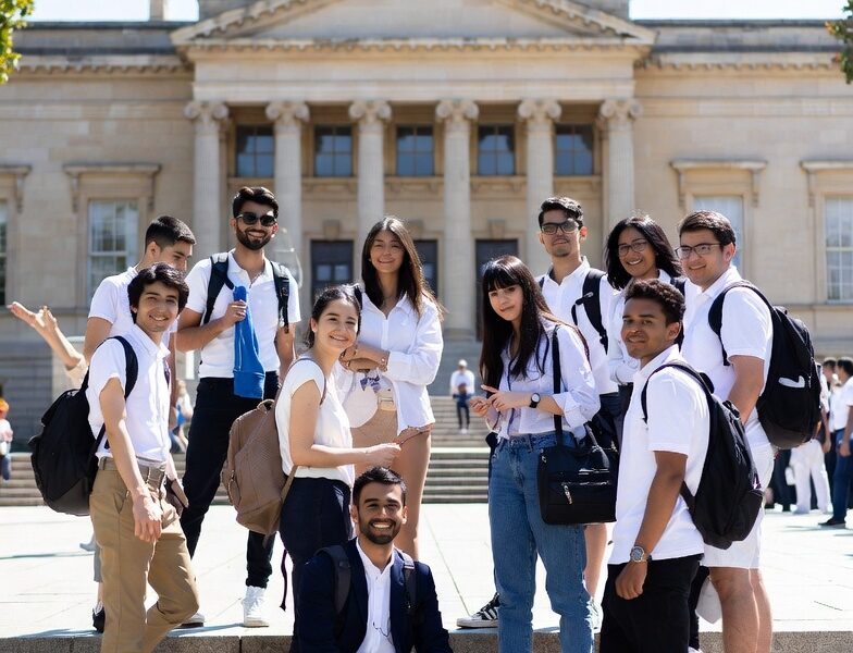 Diverse group of happy international students smiling on university steps, representing affordable countries to study abroad in 2025.