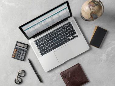 A professional laptop displaying international cost-of-living calculations alongside a passport and a wallet on a modern desk.