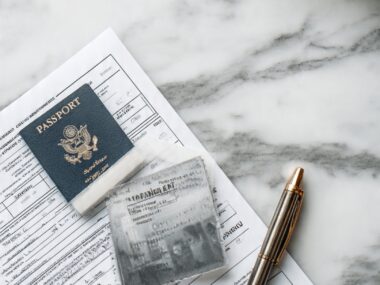 A passport, passport application form, identification document, and pen on a desk, representing the process of applying for a passport in 2026.
