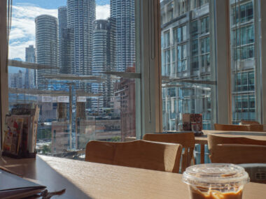 Laptop on a café table overlooking Kuala Lumpur's Petronas Twin Towers, representing study abroad in Malaysia for international students.